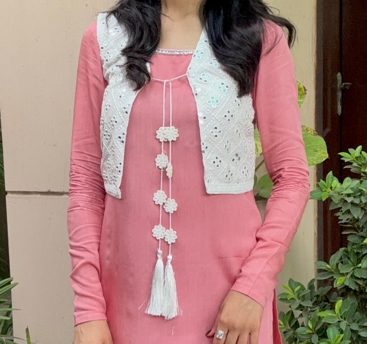 A woman wearing a pink traditional outfit with a white embroidered vest and matching pink trouser